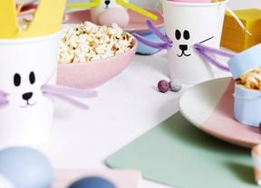 Craft cups with bunny faces on them next to a bowl of popcorn and decorative eggs.