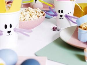 Craft cups with bunny faces on them next to a bowl of popcorn and decorative eggs.