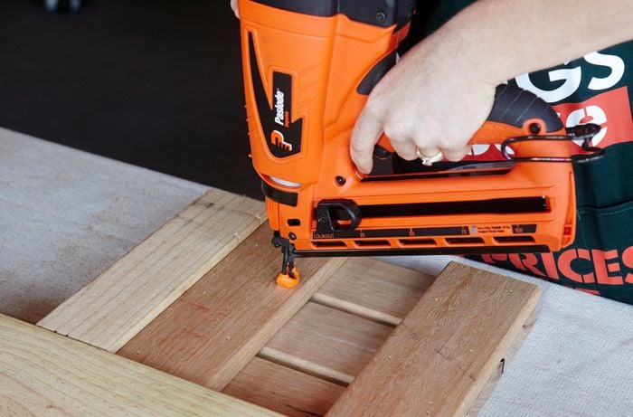 A person attaching pieces of timber using a nail gun