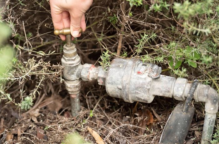 A person is turning off the water supply at an isolation valve to help prevent unexpected leaks or water sprays while replacing a shower head.
