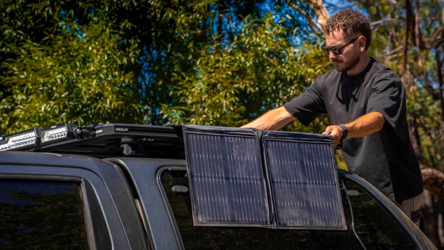 Person setting up the KT Solar 300W Solar Folding Blanket beside a 4WD vehicle outdoors.