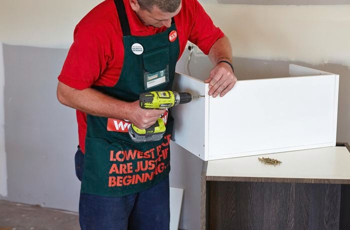 A person attaching the sides of a cabinet using a cordless driver