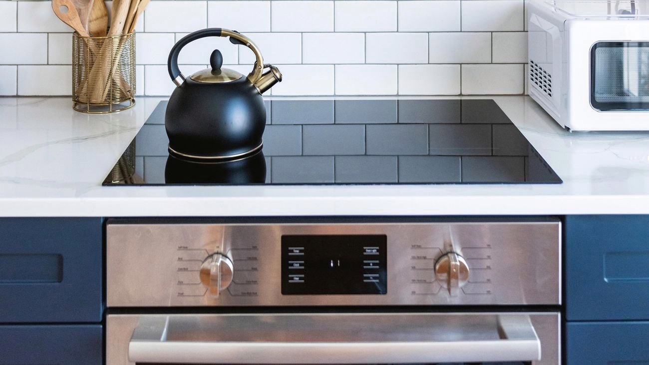 Stove with silver extractor fan with a black kettle sitting on the stove top