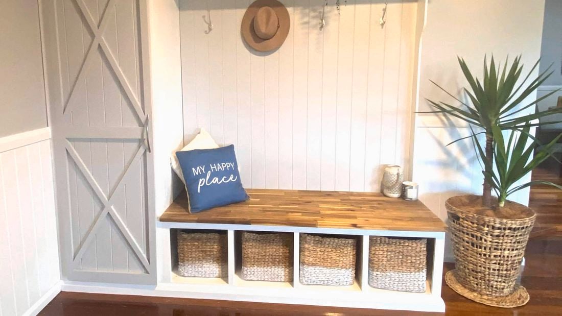 Built‑in mudroom bench with storage baskets, timber seat and a plant beside it.