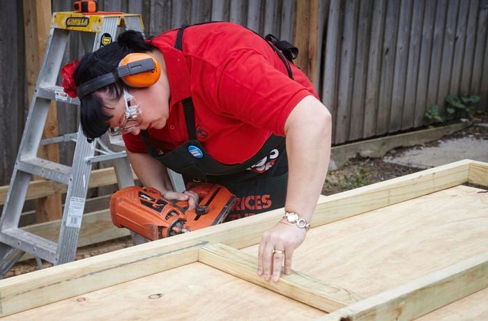 A person wearing protective gear attaching parts of a timber frame using nail gun