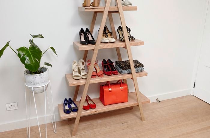 A completed shoe storage rack against a white wall holding ten pairs of ladies shoes, two picnic blankets and a handbag