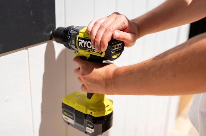   A person is mounting a chalkboard wall panel using screws and a drill. 