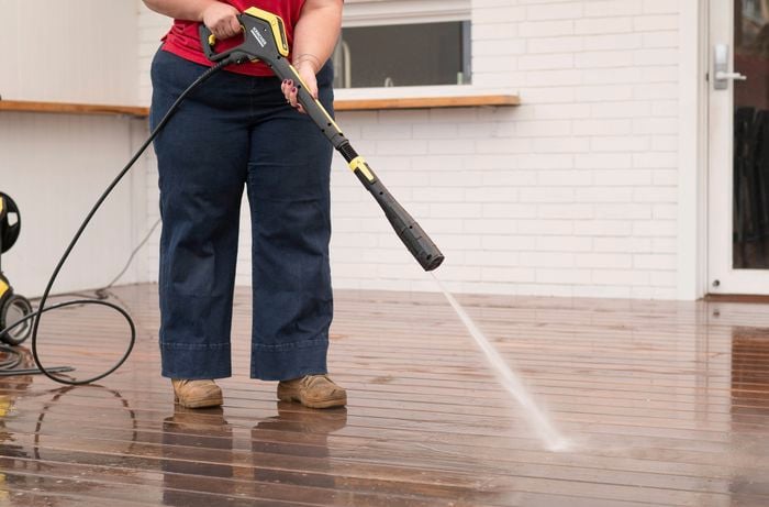 A person is using a Karcher pressure washer to rinse off the cleaning solution from the deck.