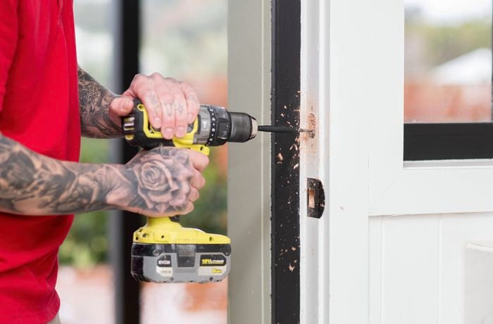 A person is drilling into a door frame to create a hole for the strike plate installation