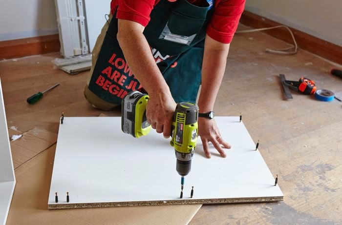 A person inserting pins into a cabinet panel using a cordless drill