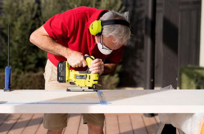 A Bunnings Team Member is using a jigsaw to carefully cut the corners along a marked line on a benchtop. 