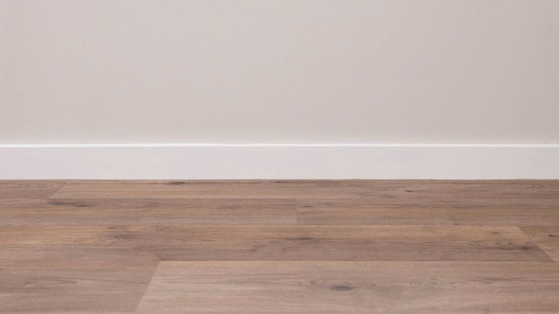 A clean, finished white skirting board neatly installed above a wooden floor.