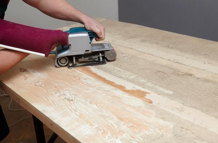 A wooden tabletop being sanded with a belt sander