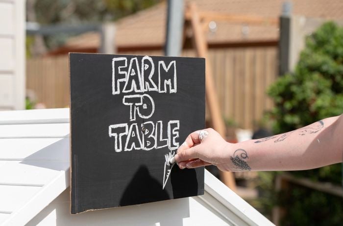 A sign mounted on a cubby house having 'farm to table' written on it with chalk