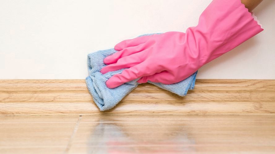 Gloved hand using a micro-fibre cloth to wipe skirting boards.