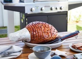 Christmas ham sitting on outdoor dining table with BBQ visible in the background.
