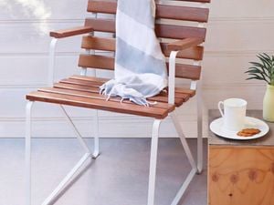 An outdoor chair with slates, sitting next to a table with a tea cup and biscuit.
