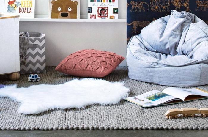 Rug with bean bag, toy box, toys and pillow on it.