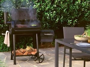 A black offset smoker barbecue with beef brisket and vegetables cooking inside, with firewood stored underneath.
