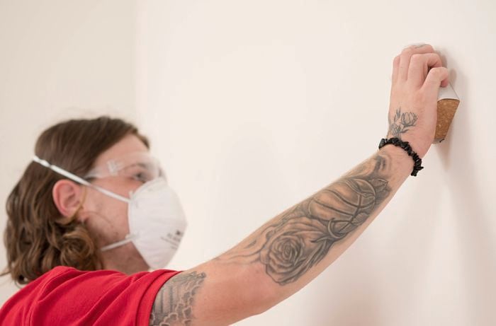 A person is sanding the walls using a sanding block.