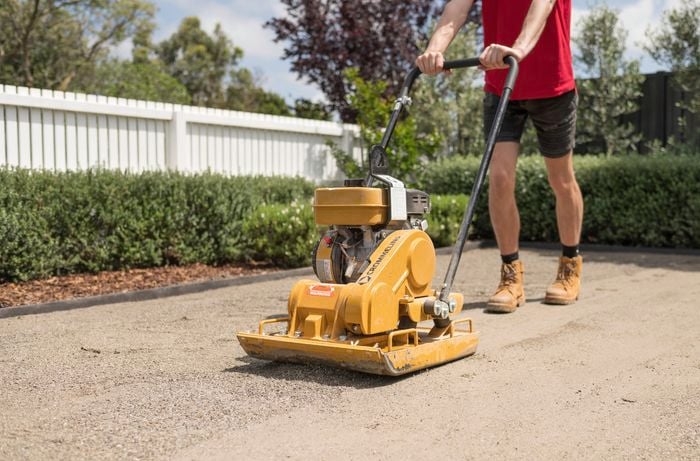 A person is using a compactor to level and compress the crusher dust layer in preparation for synthetic turf installation