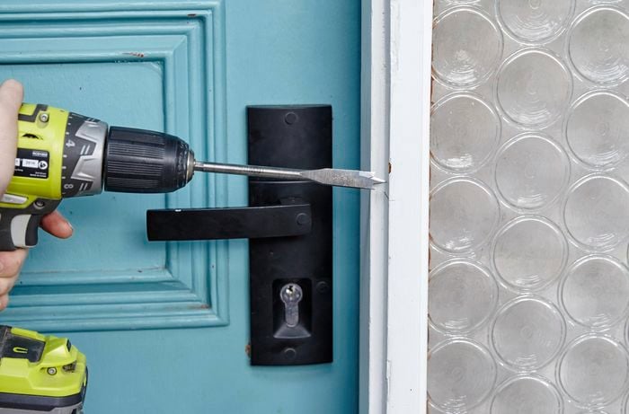 A bore spade drill bit being used to gouge a hole for the security door's striker in the door frame