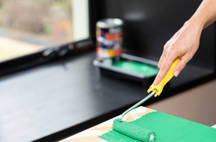 A person is using a paint roller to apply green base coat across the canvas to make a grassy background. 