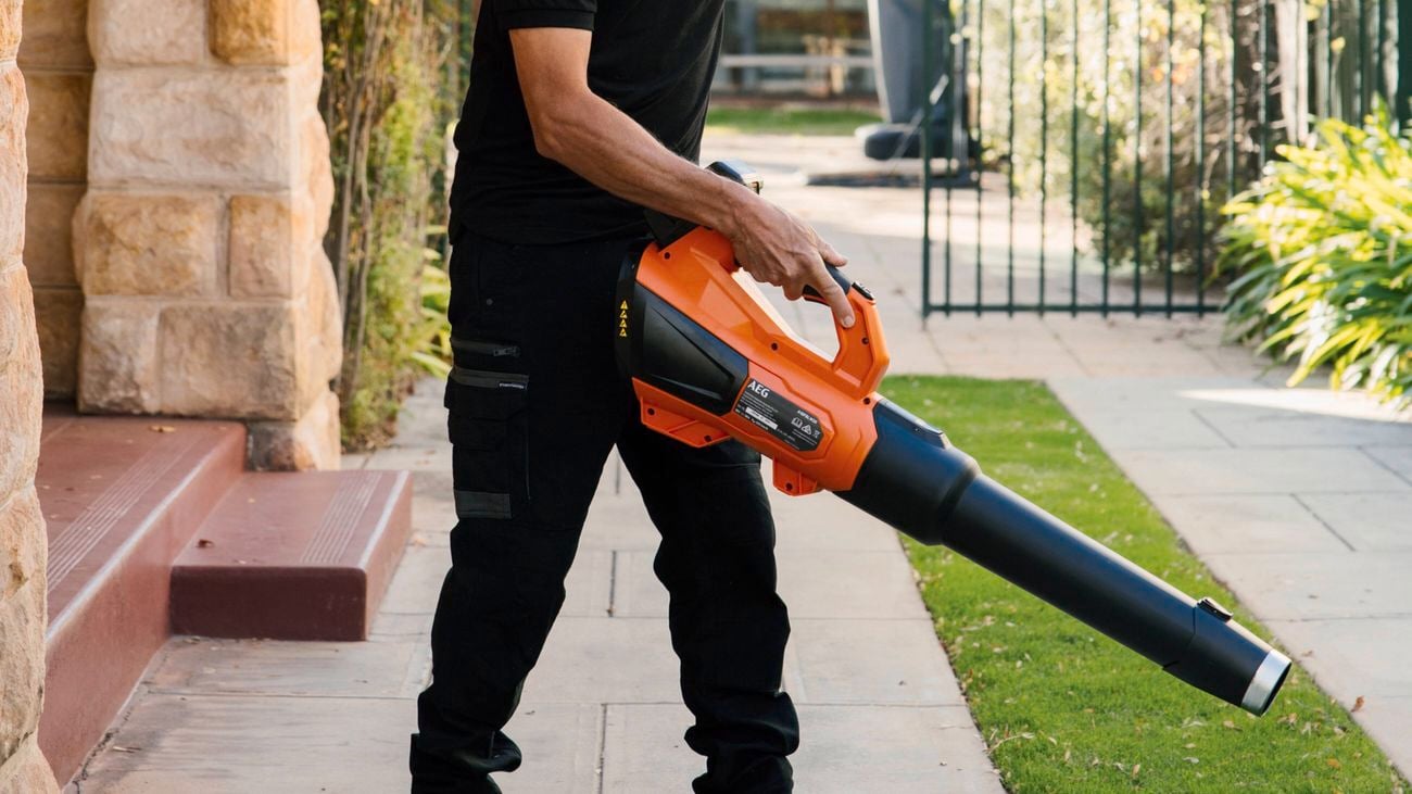 A close up image of a man photographed from the shoulders down using a AEG 18V Fusion Stealth jet blower in a garden setting