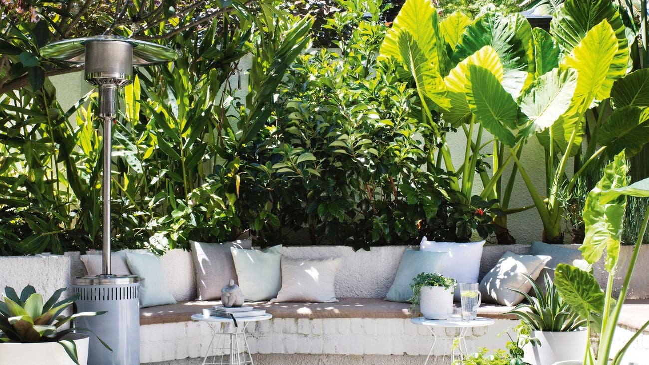 An outdoor built-in bench seat surrounded by plants both potted and planted in a garden bed.
