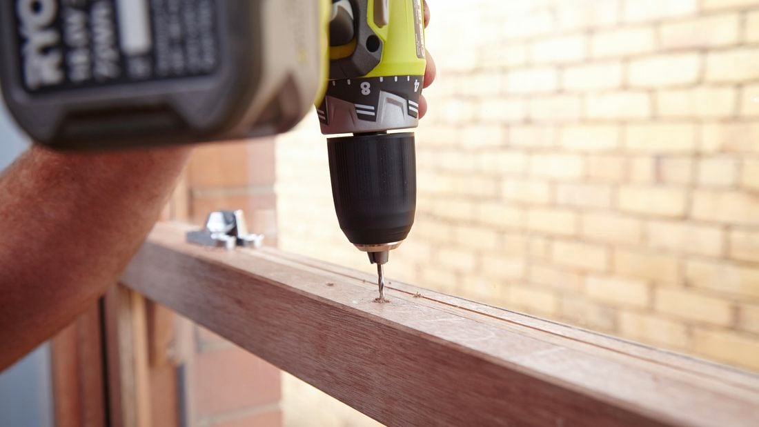 Person using a cordless drill to drill a hole in a sash window frame