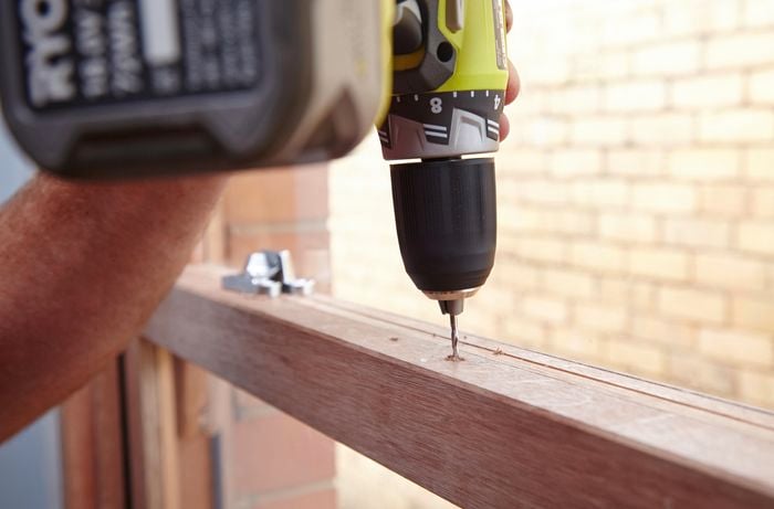 Person using a cordless drill to drill a hole in a sash window frame