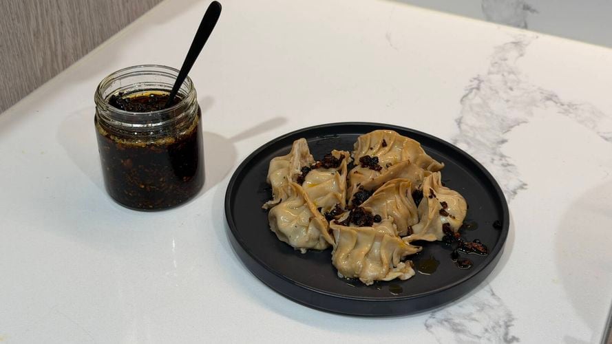 Plate of dumplings drizzled with homemade chilli oil beside a jar of chilli oil on a kitchen benchtop.