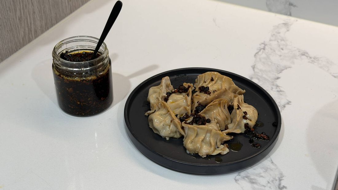 Plate of dumplings drizzled with homemade chilli oil beside a jar of chilli oil on a kitchen benchtop.