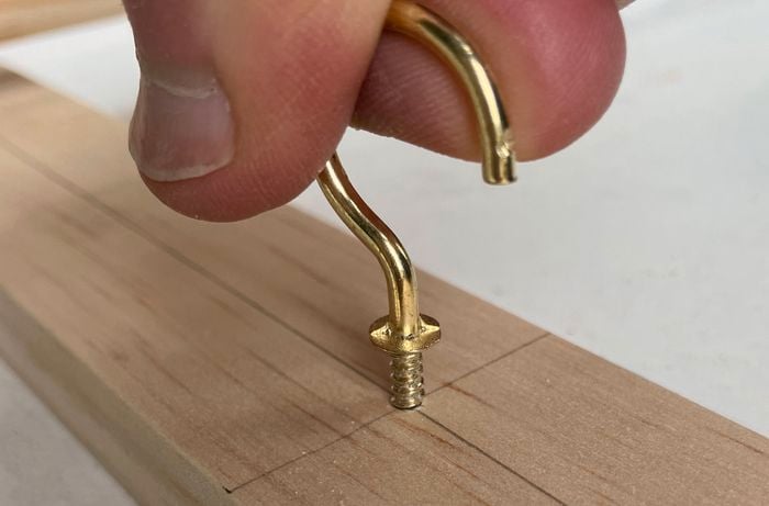 Close up of a hand screwing a cup hook into a slat of dressed pine
