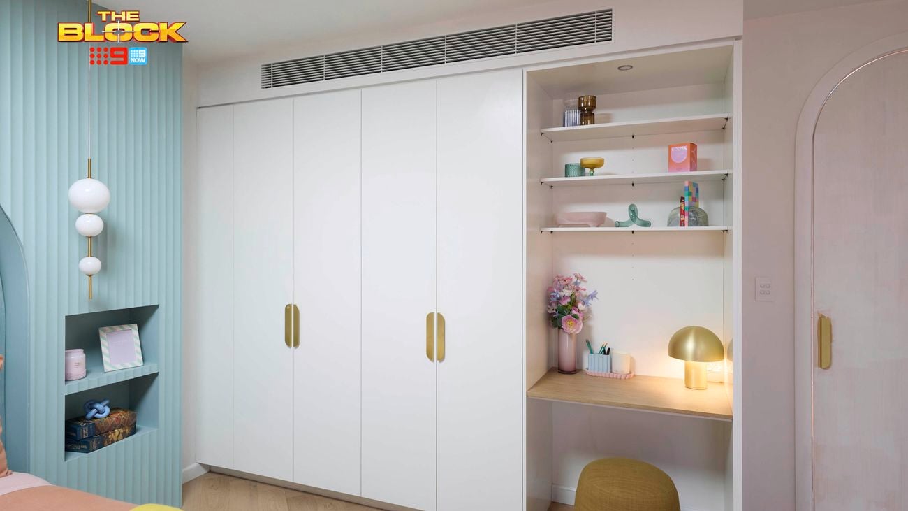 Pastel bedroom featuring a pale blue feature wall with recessed bedside tables and a wardrobe and desk.