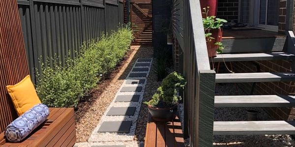 Garden area with lawn and pavers, next to timber bench seating leading down the side of the house to a front gate