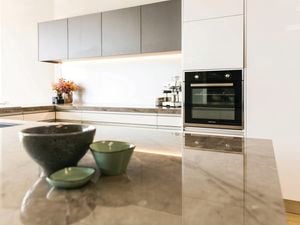 White modern kitchen with a marble benchtop with crockery on it, grey cupboards, and an oven in it.