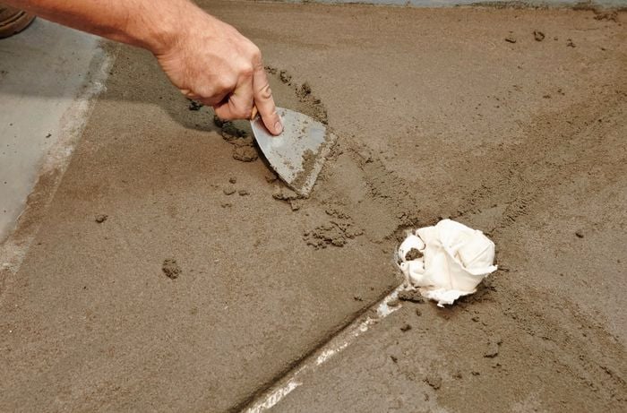 A person using a paint scraper to fill gaps with screed