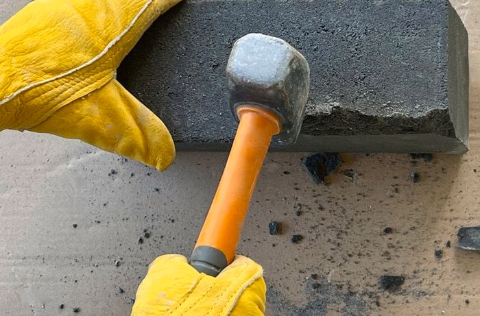A person uses a club hammer to remove the retaining lips from retaining wall blocks