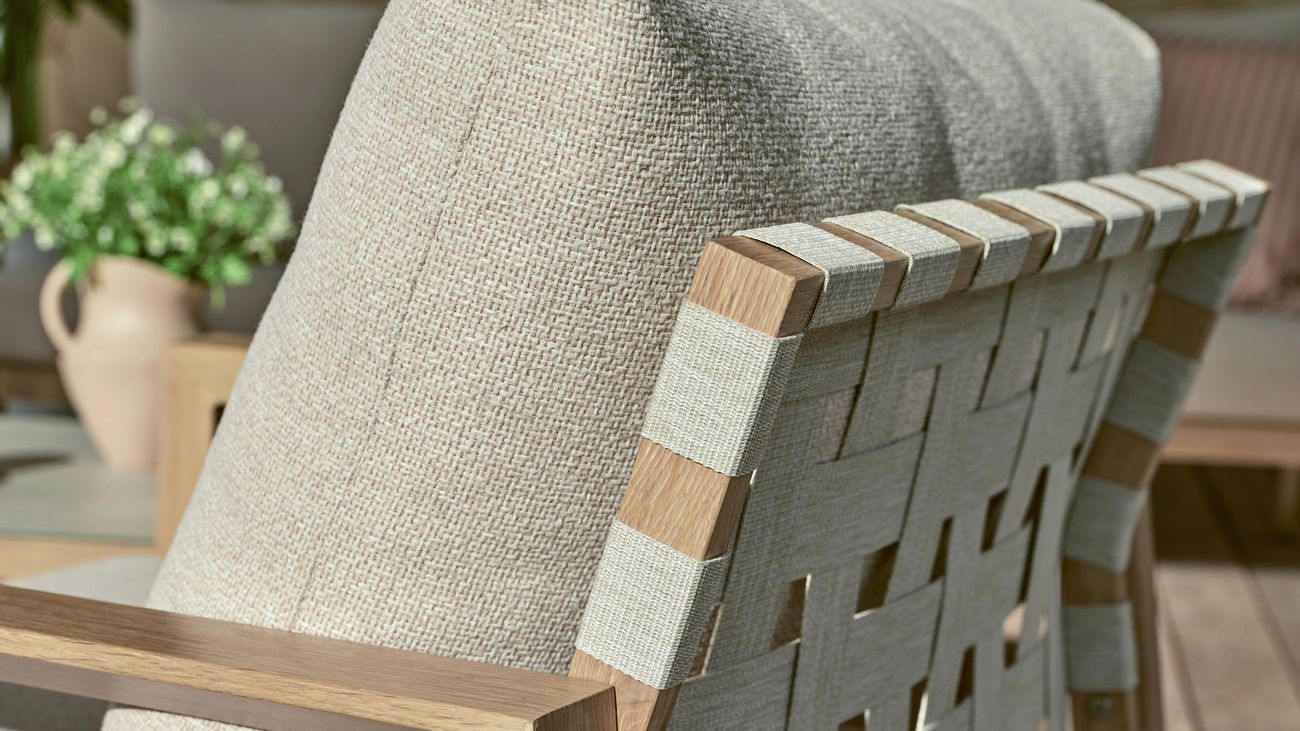 Timber-framed outdoor armchair with woven fabric back and light cushions.