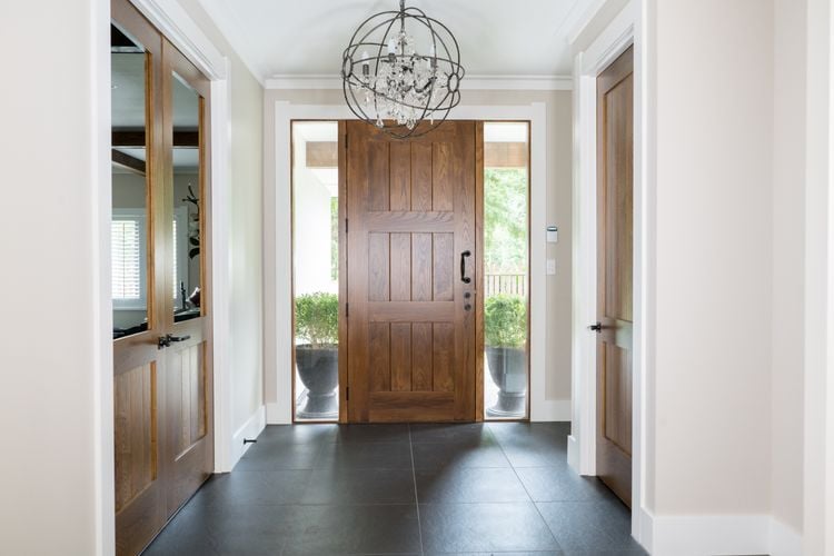 Large wooden entrance door in entryway with dark tiles and a light fixture
