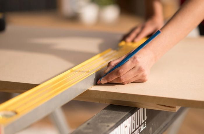 Marking lines on a wooden board using a straightedge and a pencil.