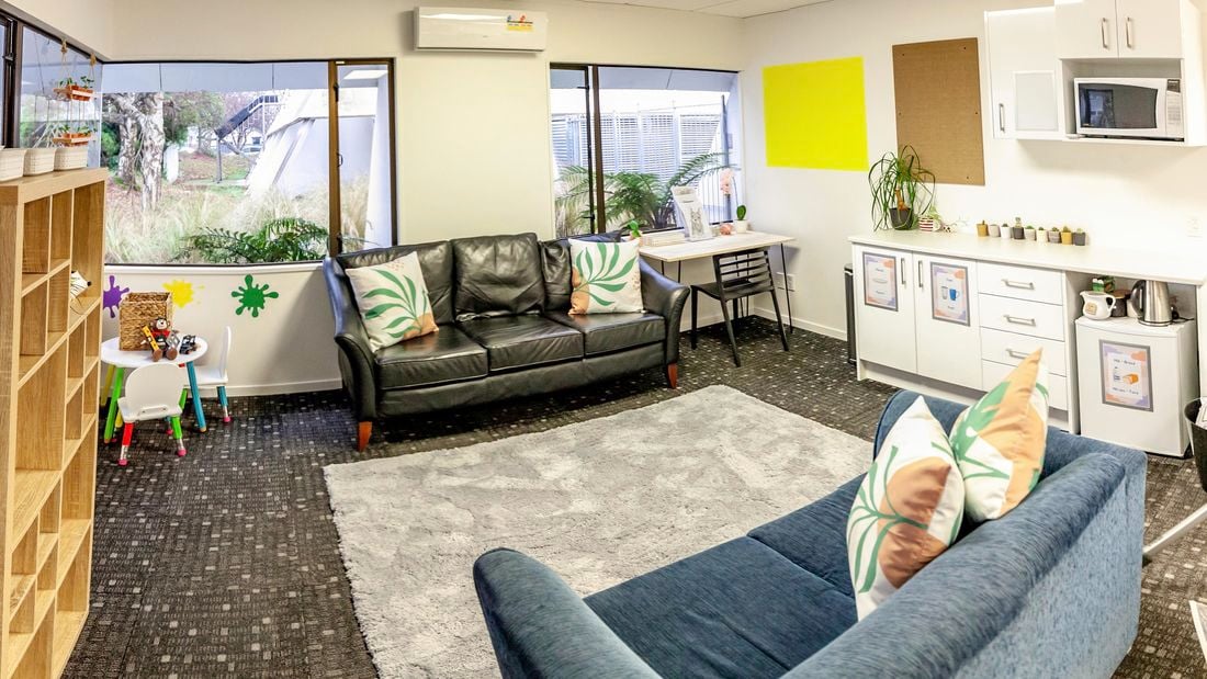 A room with 2 x couches, table with chairs and a bookcase next to a wall