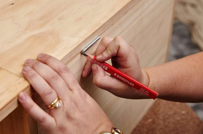 Hinges being used as a guide to mark a timber storage bench for screw holes later