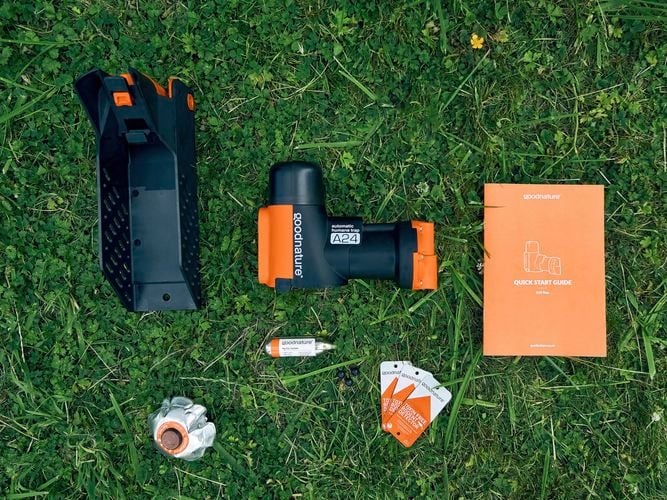 A flatlay of everything that comes with an A24 smart trap laid out on the grass