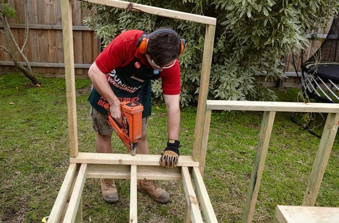 The roosting box base being attached to the supports below by a Bunnings team member with a nail gun
