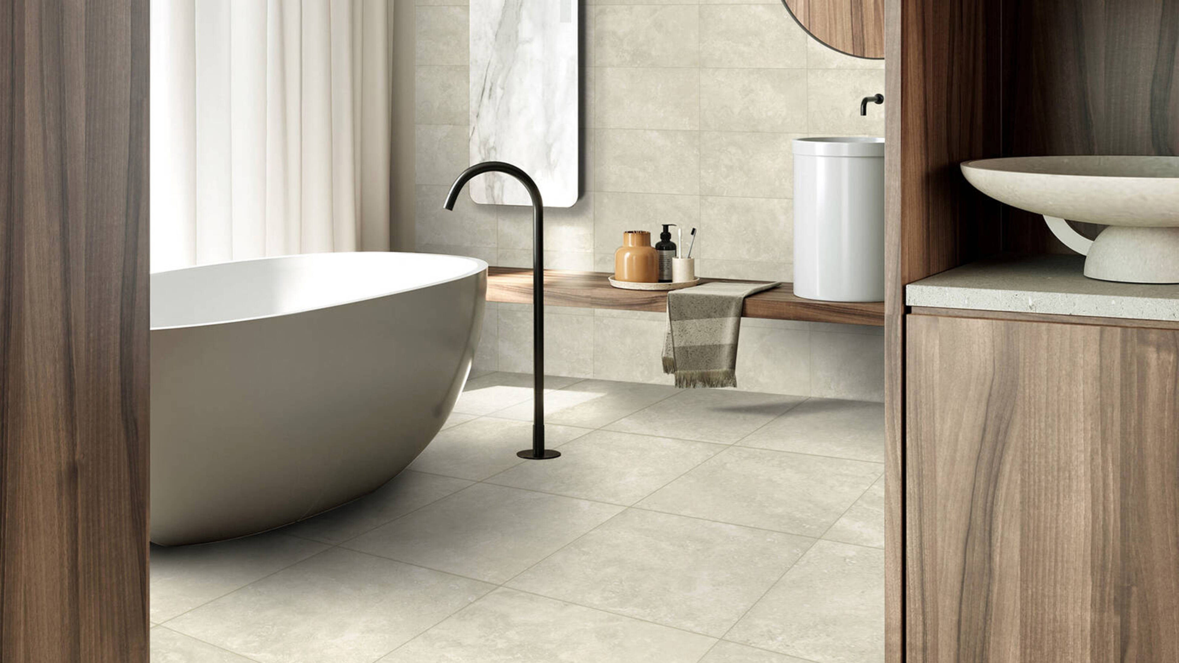 A modern bathroom with a white freestanding bathtub, black tap, light tiles, and a wooden vanity with a white basin and wooden cabinetry