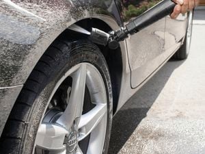 Washing car wheels using pressure washer on driveway