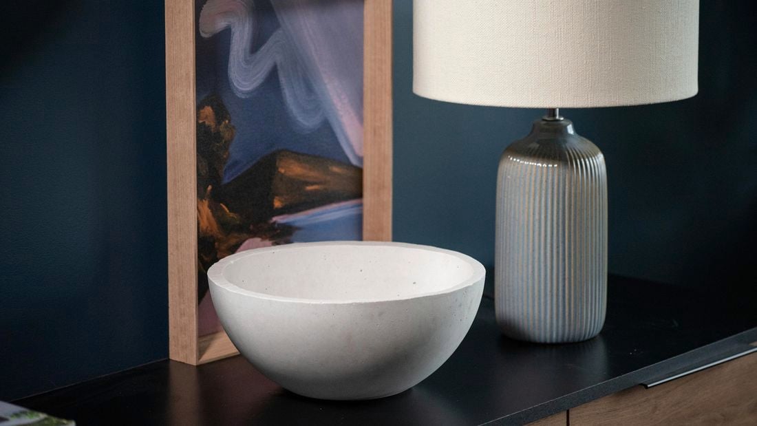 white bowl sitting on a cabinet, with a  white lamp and print in the back ground