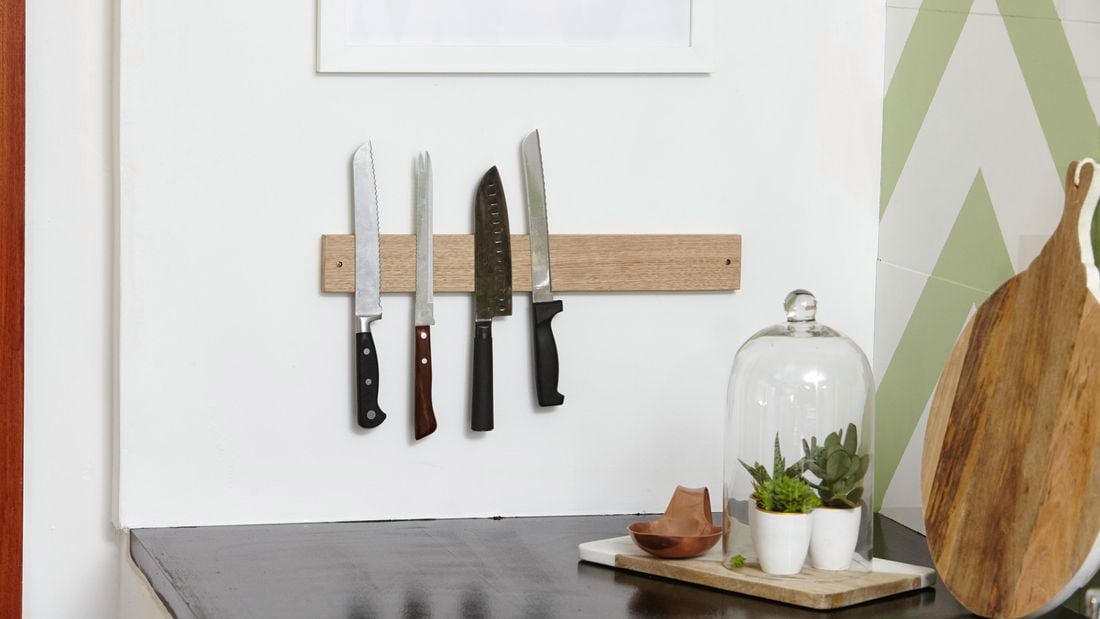 A kitchen with a black benchtop and knives on a magnetic rack on the wall
